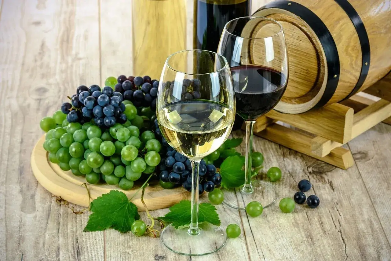 Zwei Gläser Wein, Trauben und ein Holzfass – perfekt für das Kochen mit Alkohol.