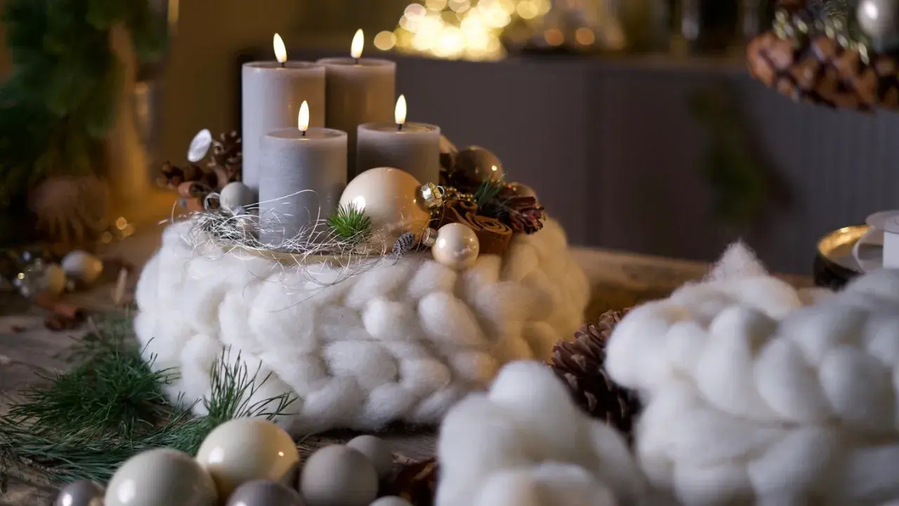 Ein Adventskranz mit vier grauen Kerzen, umwickelt mit dicker, weißer Wolle, dekoriert mit Zapfen und Kugeln.