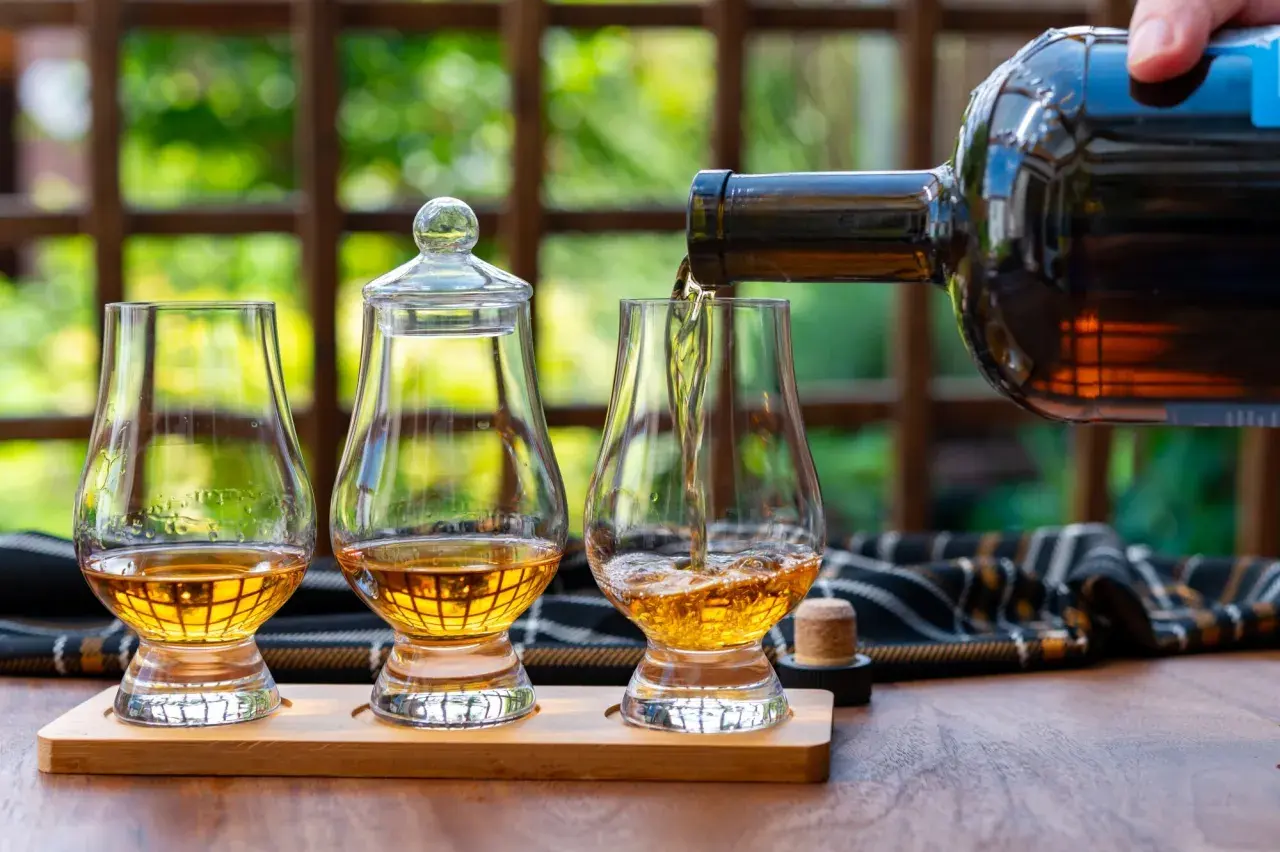 Ein Glas wird mit goldenem Whisky gefüllt, bereit, pur getrunken zu werden. Zwei weitere Gläser stehen daneben.