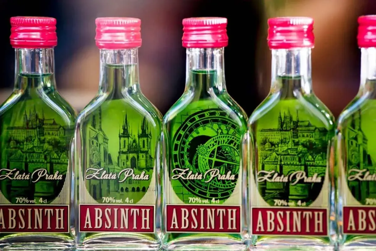 Fünf Flaschen grünen Absinths mit roten Kappen, jede mit einem Etikett, das Prag und die Aufschrift "Absinth" zeigt.