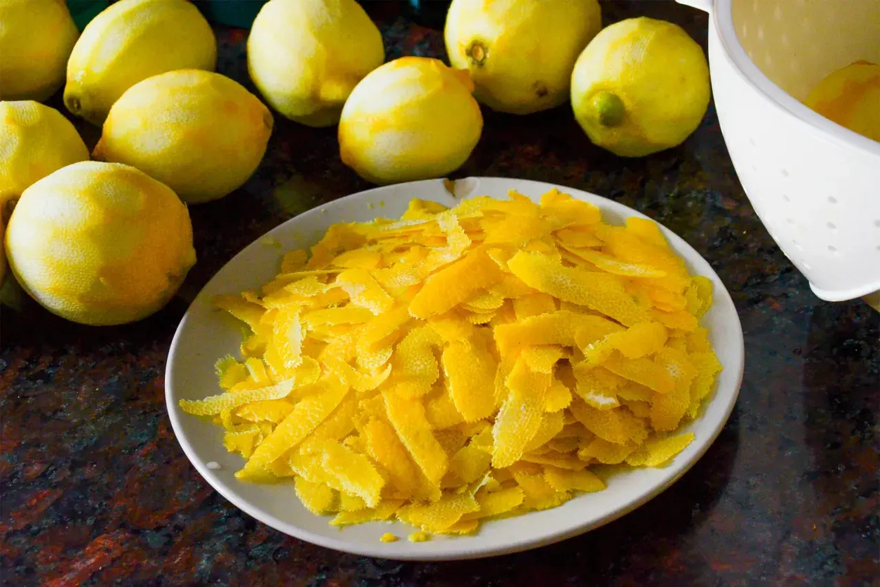 Zitronenschalen liegen auf einem Teller, bereit, um Limoncello herzustellen. Mehrere ganze Zitronen sind im Hintergrund zu sehen.