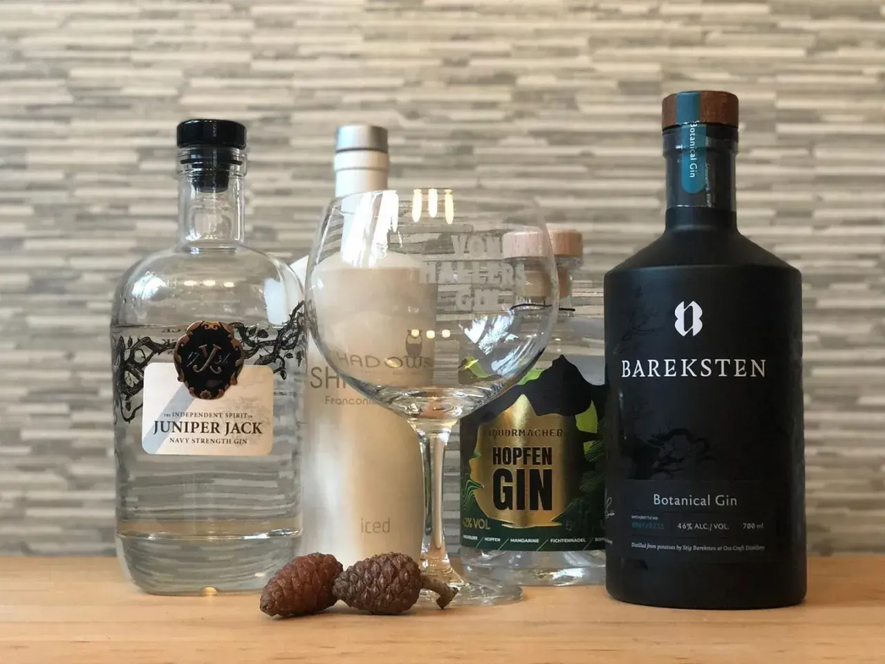 Mehrere Flaschen Gin, darunter Juniper Jack und Bareksten Botanical Gin, stehen neben einem leeren Glas und Zapfen.