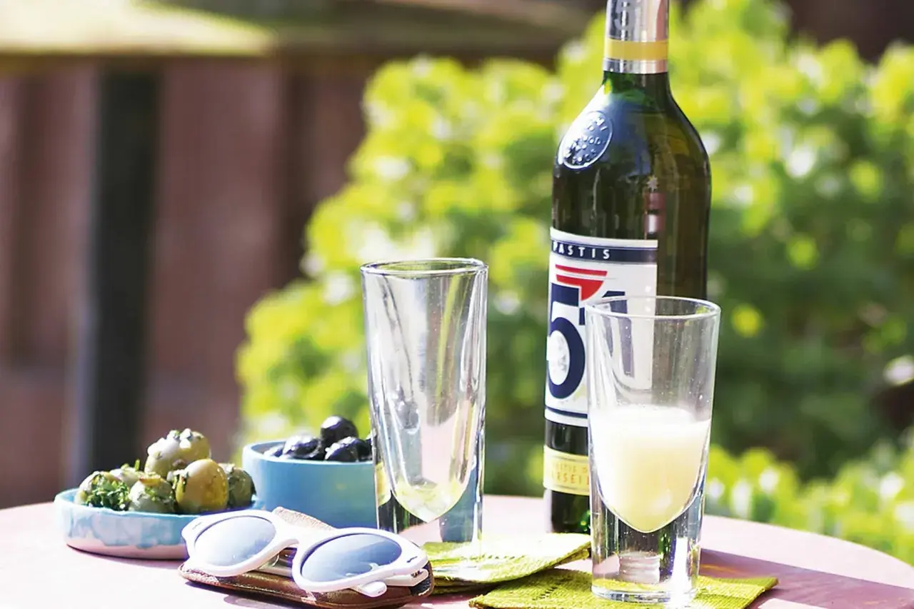 Ein Glas Pastis mit Anis Geschmack, Oliven und Sonnenbrille auf einem Tisch im Freien.