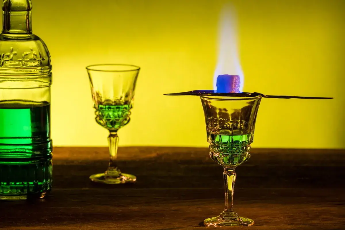 Grüner Absinth brennt über einem Zuckerwürfel in einem Glas. Die Zubereitung lässt die Absinth-Wirkung erahnen.