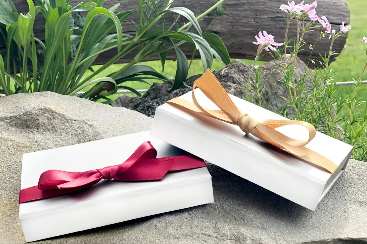 Zwei weiße Schachteln, die wie Geschenke aussehen, sind mit roten und goldenen Bändern verziert. Perfekt, um einen Gutschein in Folie zu verpacken.