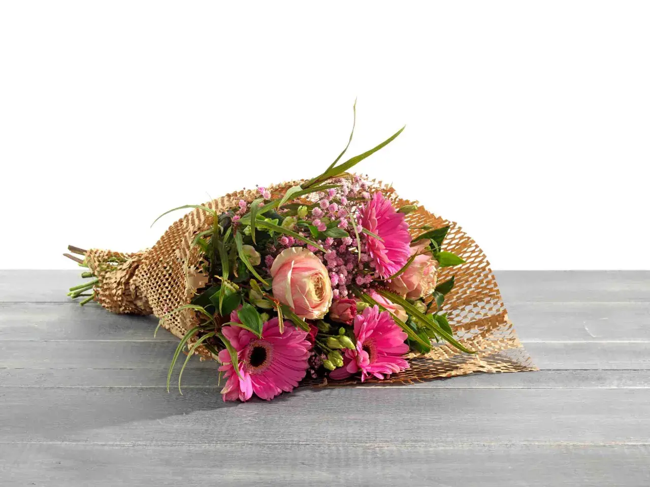 Ein Strauß bunter Blumen, liebevoll als Geschenk verpackt in braunem Papier mit Wabenstruktur, liegt auf einer Holzoberfläche.