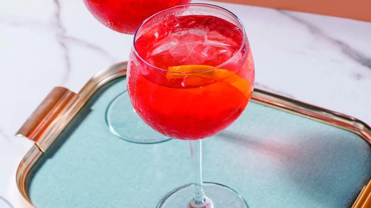 Erfrischender Campari Spritz mit Eis und Orangenscheibe auf einem Tablett.