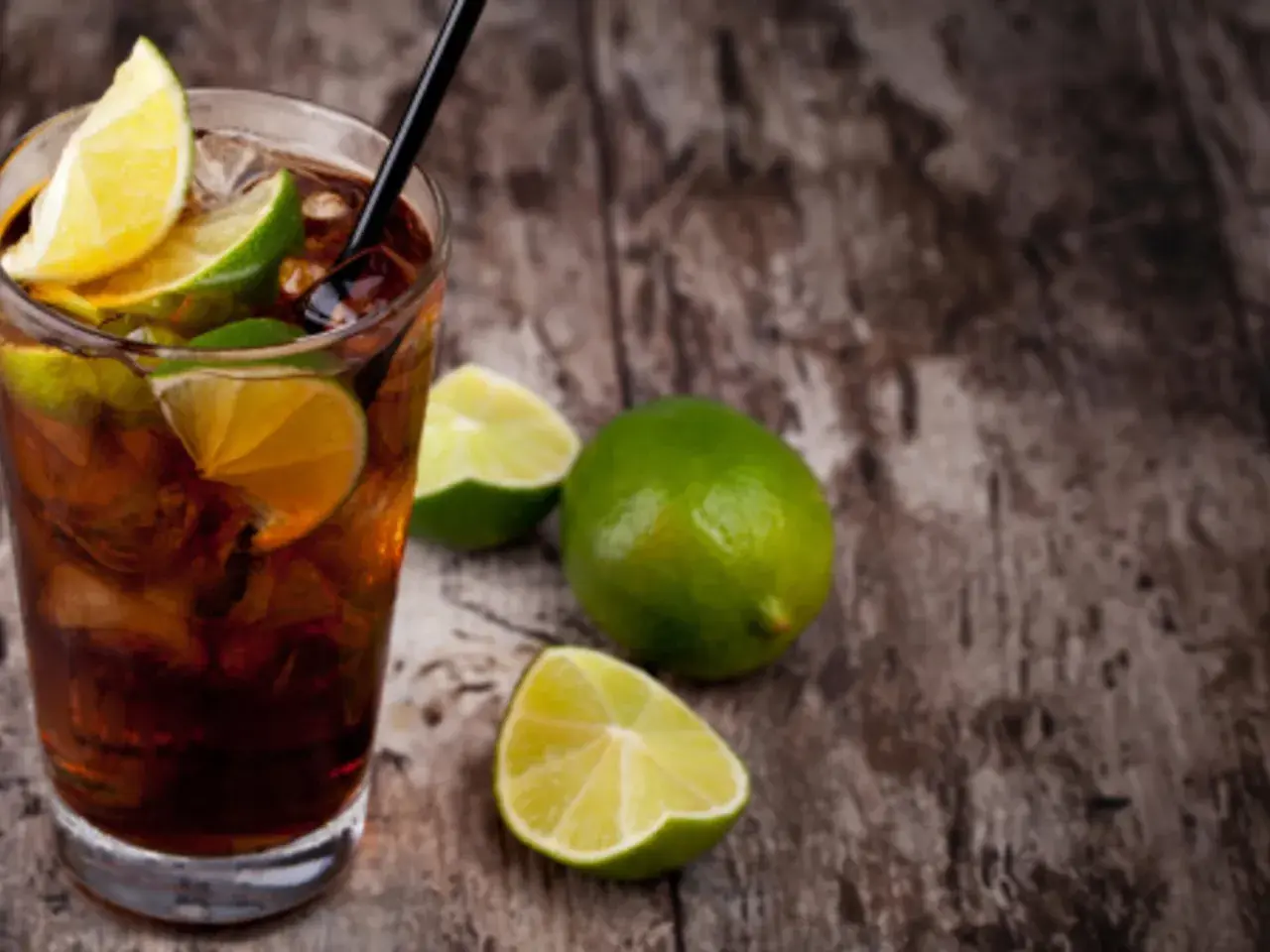 Cuba Libre mit dunklem Rum, Eis und Limettenspalten auf Holzhintergrund.