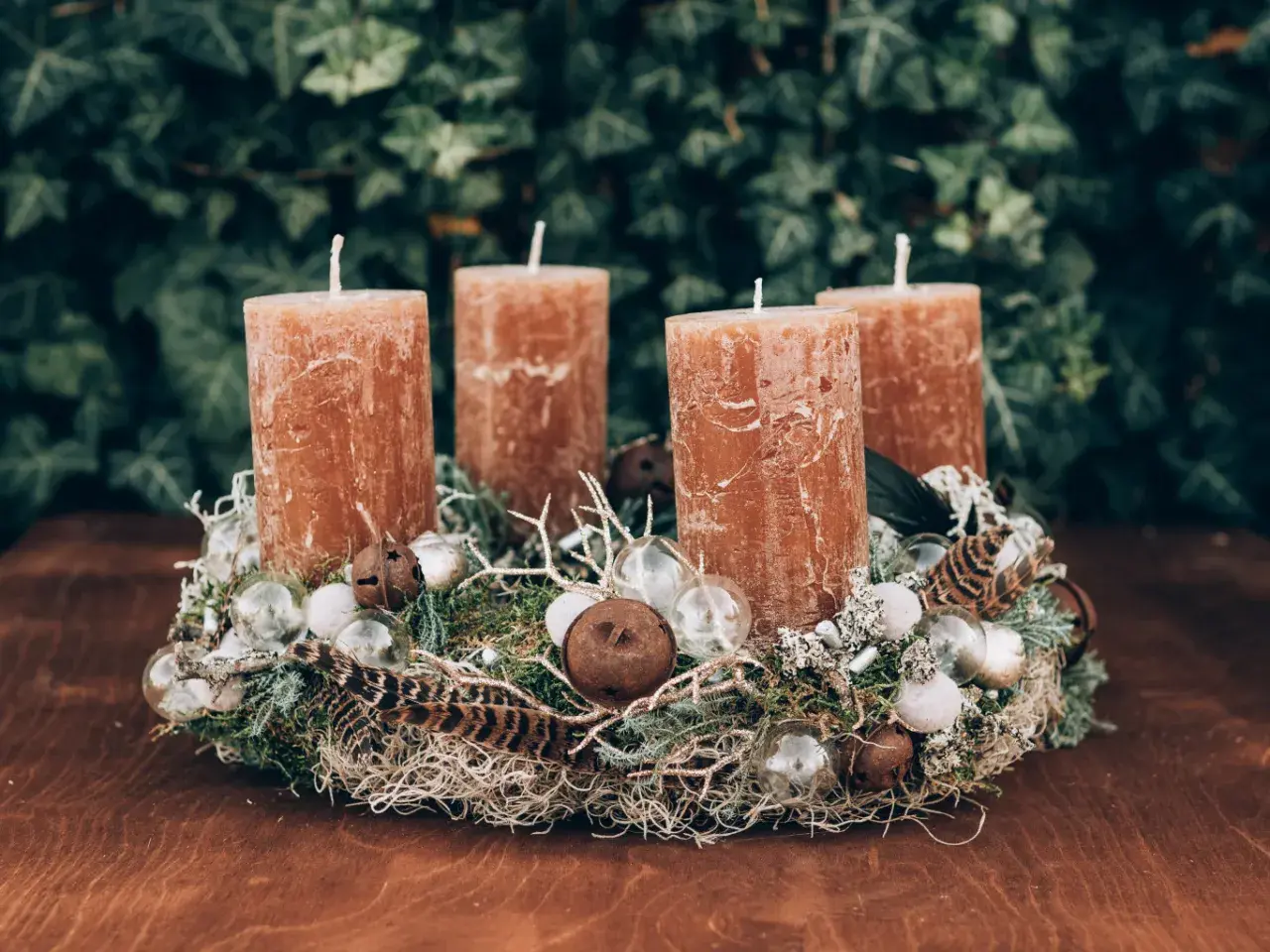 Natürlicher Adventskranz Idee mit vier braunen Kerzen, Moos, Federn und kleinen Glaskugeln auf einem Holztisch.