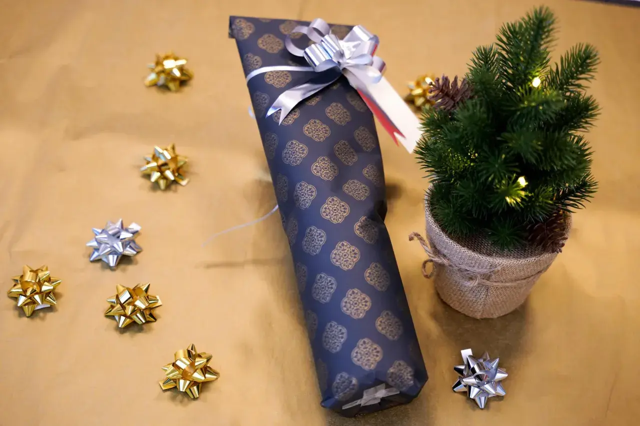 Eine **Flasche weihnachtlich verpacken** ist einfach mit diesem dunklen Geschenkpapier und silberner Schleife. Kleine Schleifen und ein Mini-Tannenbaum schmücken die Szene.