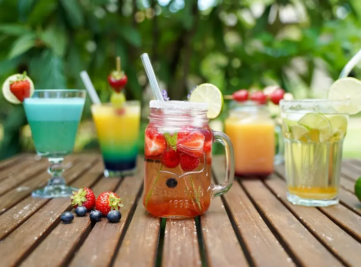 Erfrischende bunte Cocktails mit Früchten und Limette auf einer Holzoberfläche, perfekt für einen Sommertag.