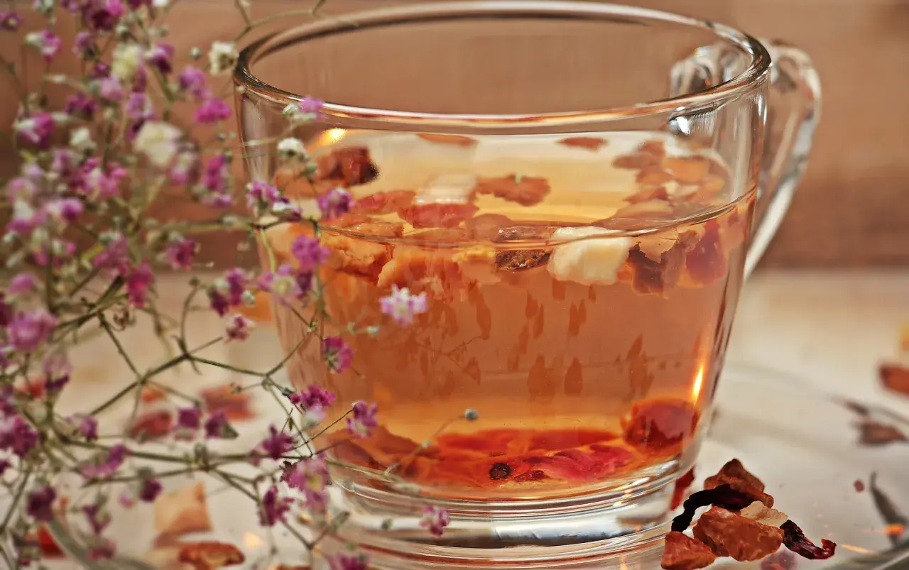Ein Glas **Tee mit Schuss** und getrockneten Früchten, umrahmt von zarten rosa Blüten.