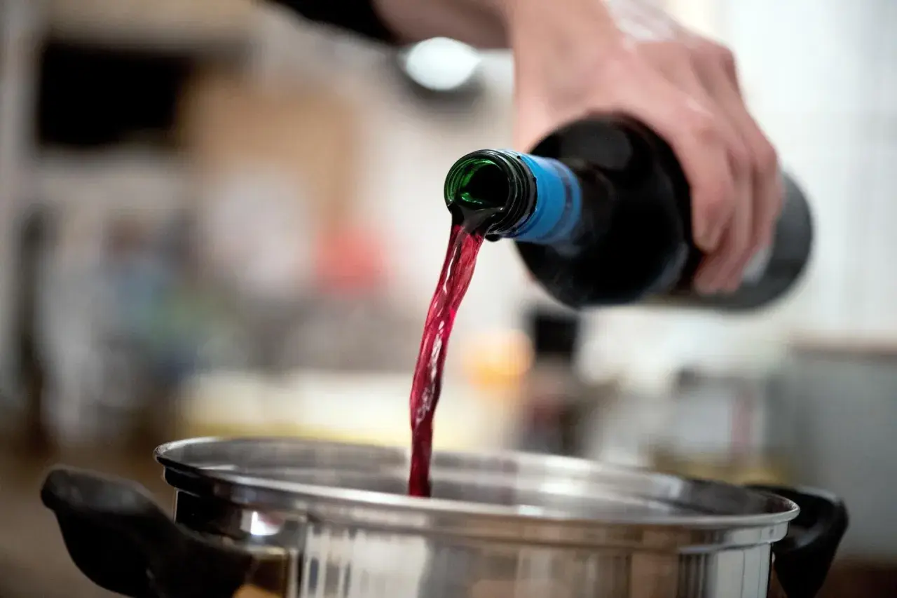 Roter Wein fließt aus einer Flasche in einen Topf. Perfekt als alkohol zum kochen für ein köstliches Gulasch.