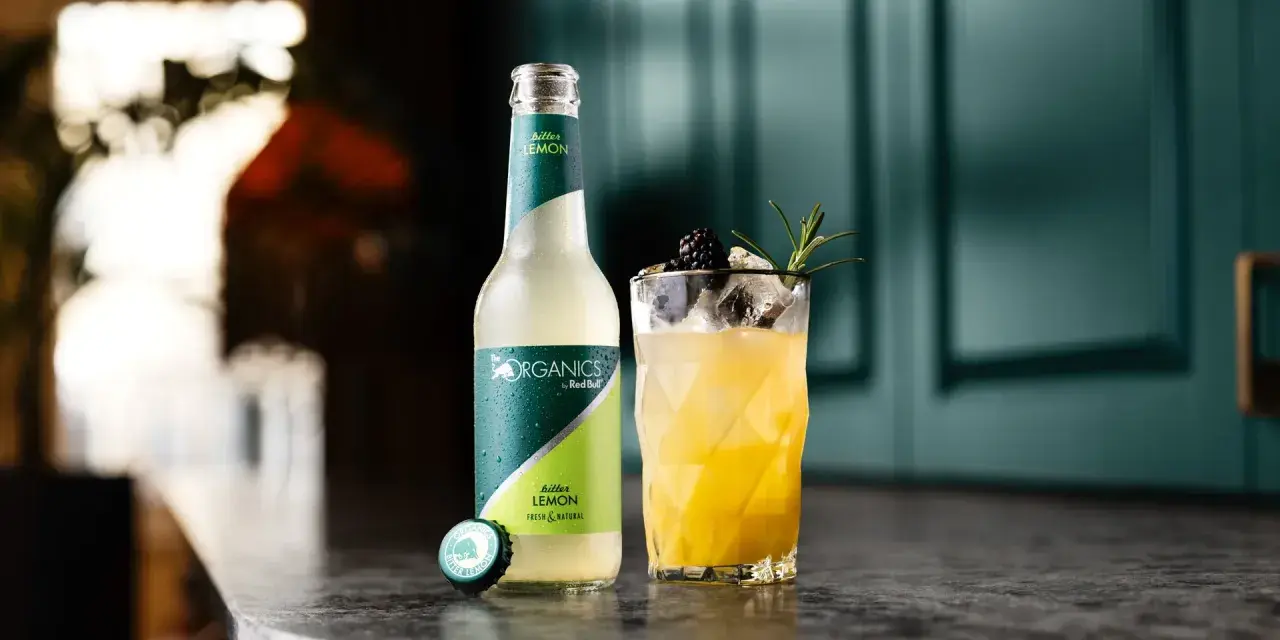Erfrischender bitter lemon cocktail mit Brombeere und Rosmarin. Daneben eine Flasche "The Organics by Red Bull Bitter Lemon".