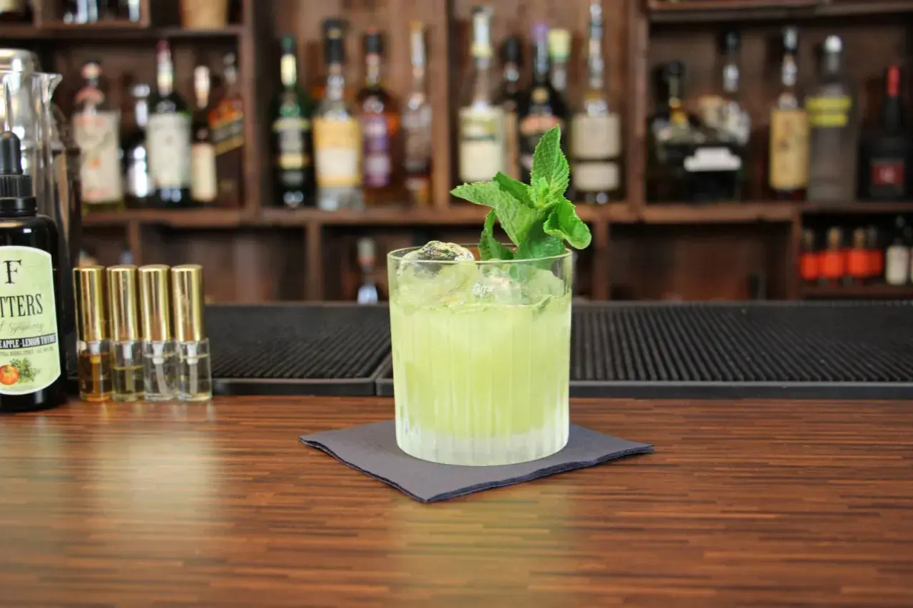 Ein erfrischender grüner Cocktail mit Minze, Eis und einer Flasche Bitters. Perfekt, um zu sehen, mit was man Tequila mischt.