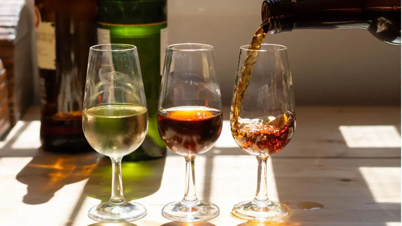 Drei Gläser mit Sherry Aperitif, eines hell, eines dunkelrot, das dritte wird gerade gefüllt.