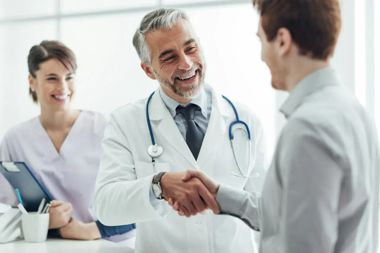 Ein Arzt schüttelt einem Patienten die Hand, ein Lächeln der Zufriedenheit. Im Hintergrund eine lächelnde Krankenschwester. Ein schönes Bild für eine Danksagung Krankenhaus.