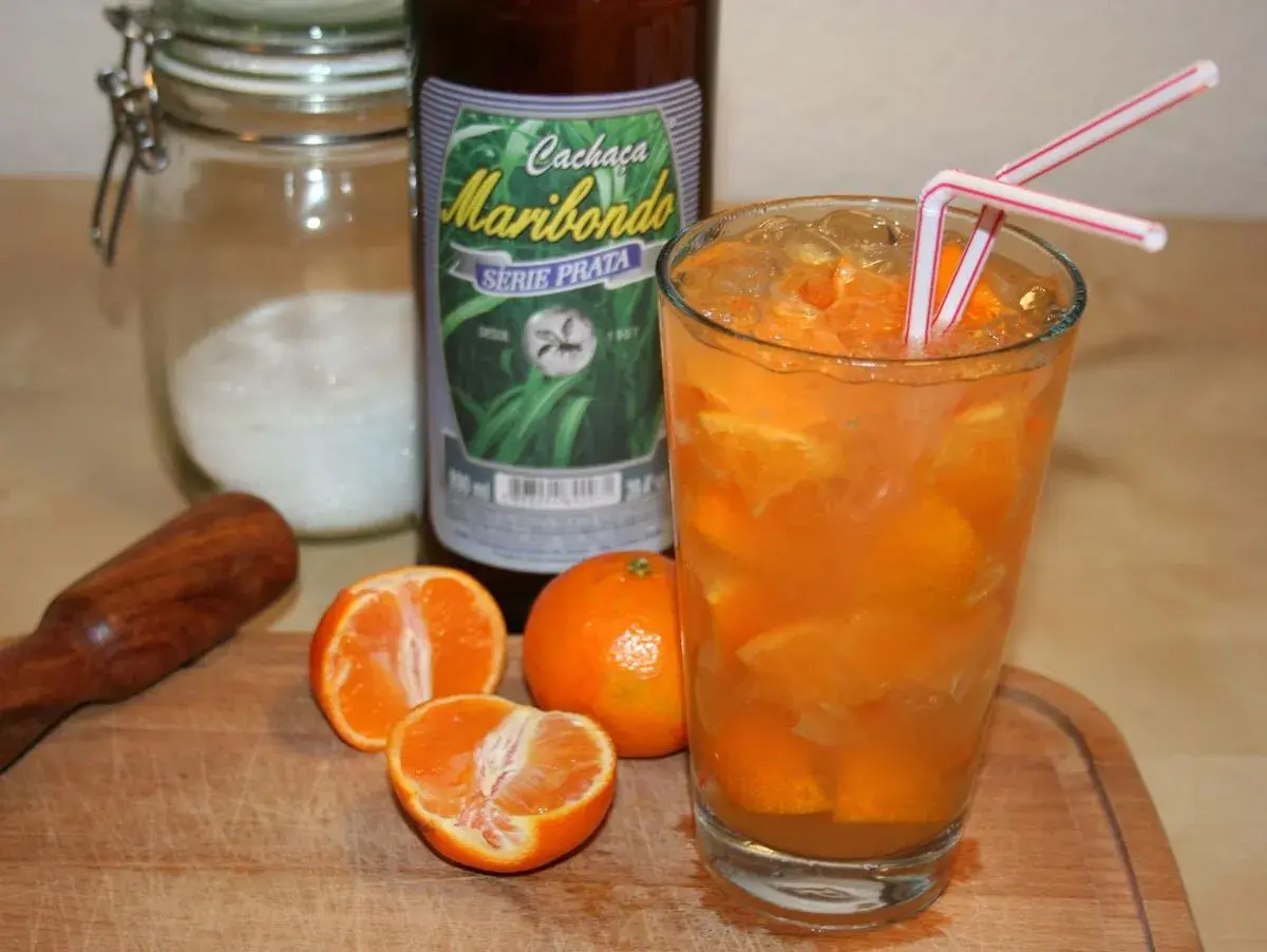 Ein Glas mit Eis und Orangenscheiben, daneben eine Flasche "Cachaça Maribondo". So wird Cachaça, ein brasilianischer Zuckerrohrschnaps, oft serviert.
