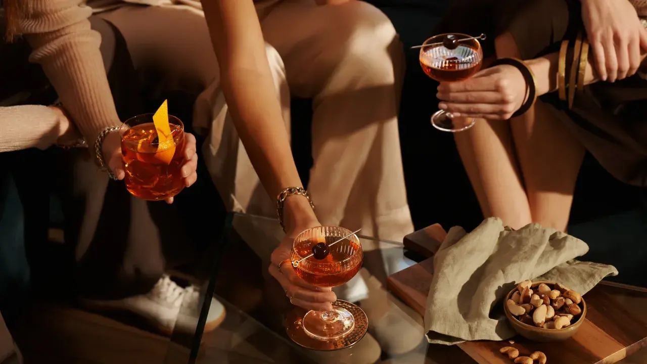 Hände halten Cocktails mit Orangen-Garnitur und Kirsche. Perfekt für den Tag des Whiskys.