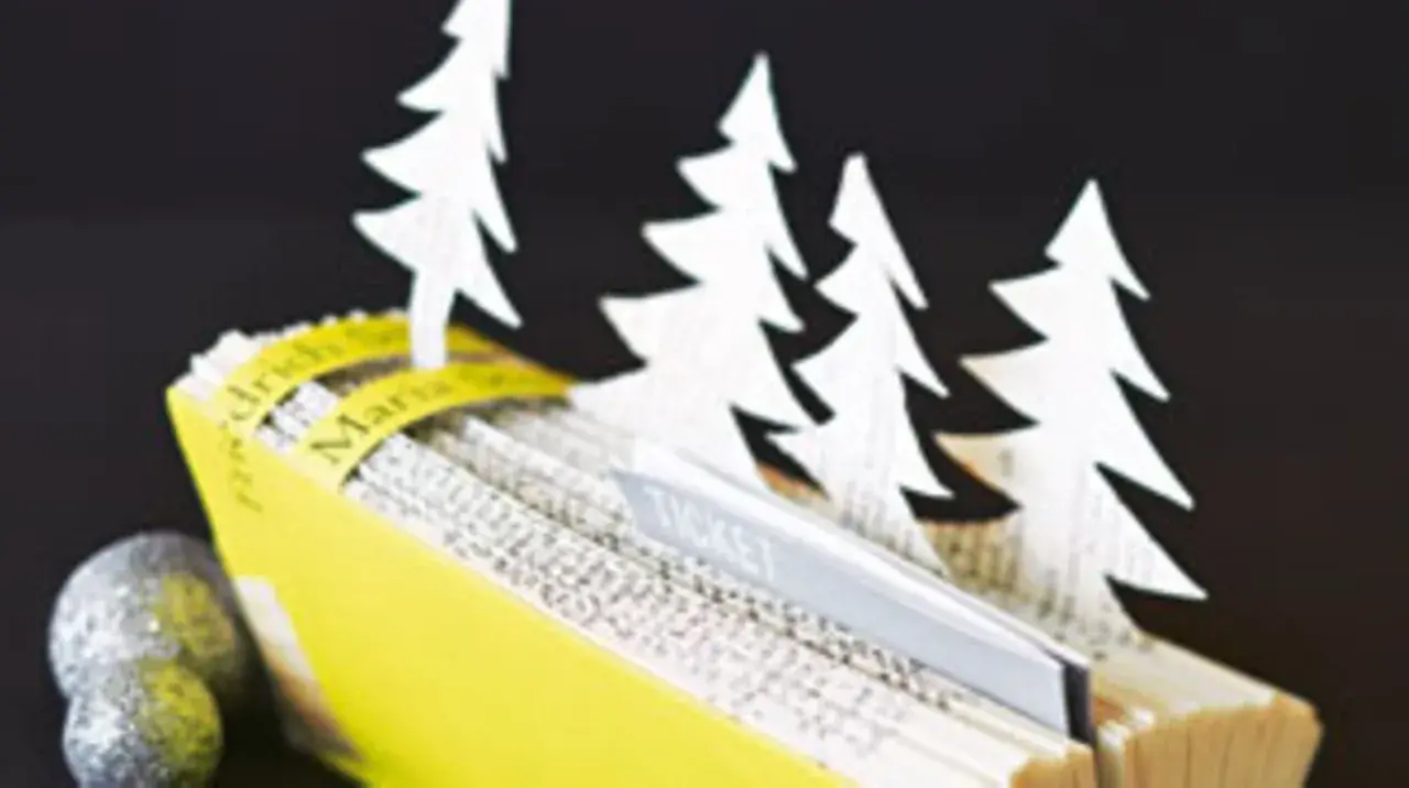 Kreative **Tickets verpacken Ideen**: Ein aufgeschlagenes Buch mit weißen Tannenbäumen und einem Ticket-Einschub, daneben glitzernde Kugeln.