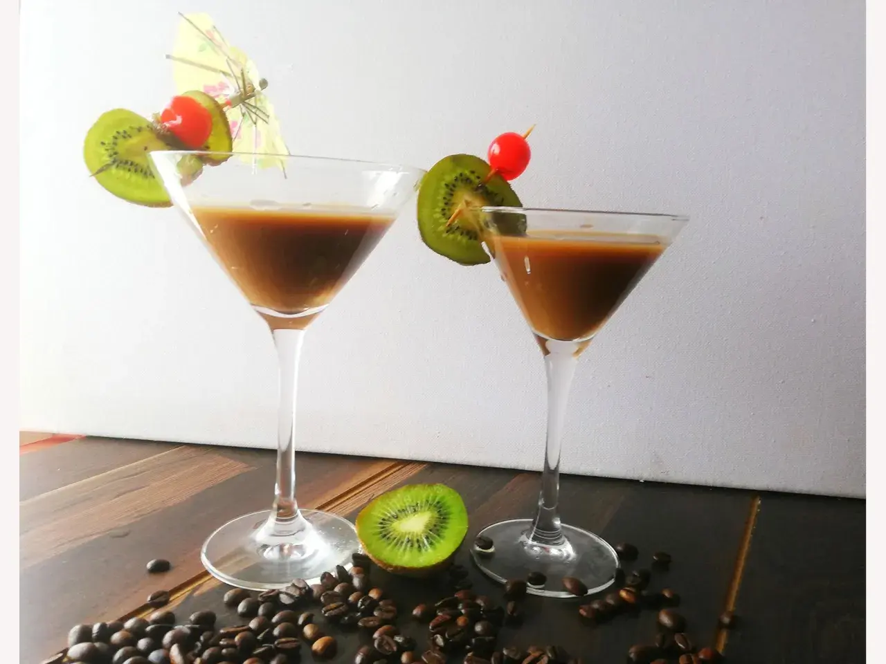 Zwei Martinigläser mit braunem Getränk, garniert mit Kiwi und Kirsche. Kaffeebohnen und eine halbe Kiwi liegen auf dem Tisch. Inspiration für Montenegro Rezepte.