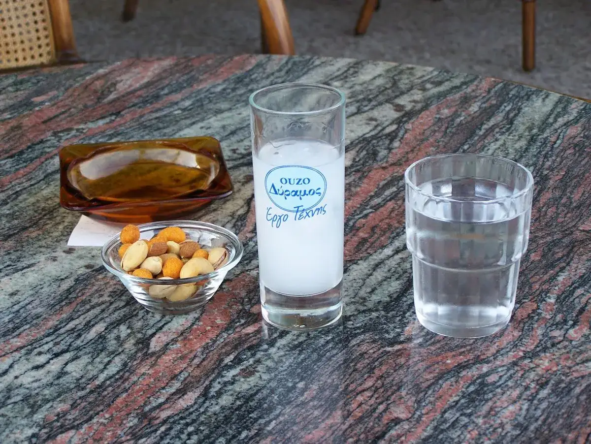Ein Glas Ouzo mit Wasser und eine Schale Nüsse auf einem Marmortisch.