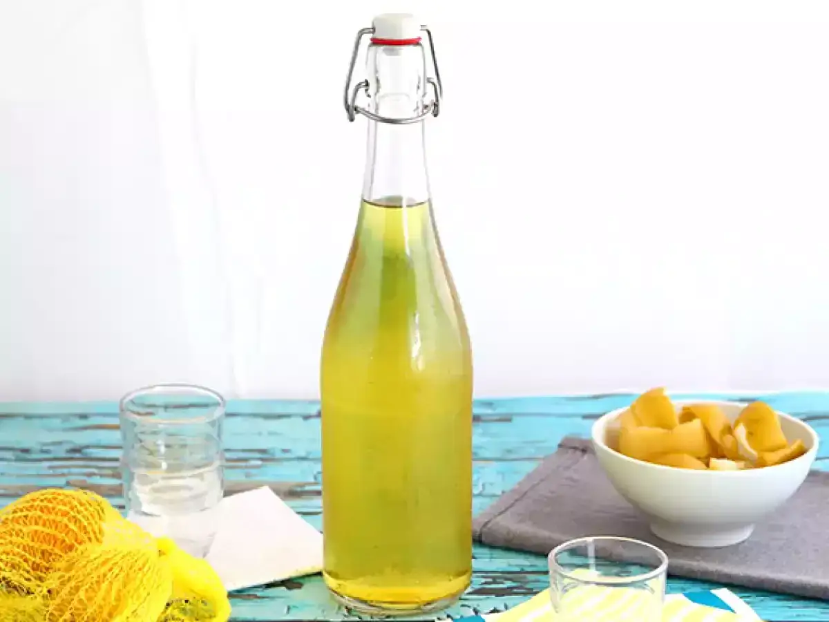 Flasche mit selbstgemachtem Limoncello, Zitronenschalen in einer Schüssel und ein Schnapsglas. Perfekt zum Limoncello herstellen.
