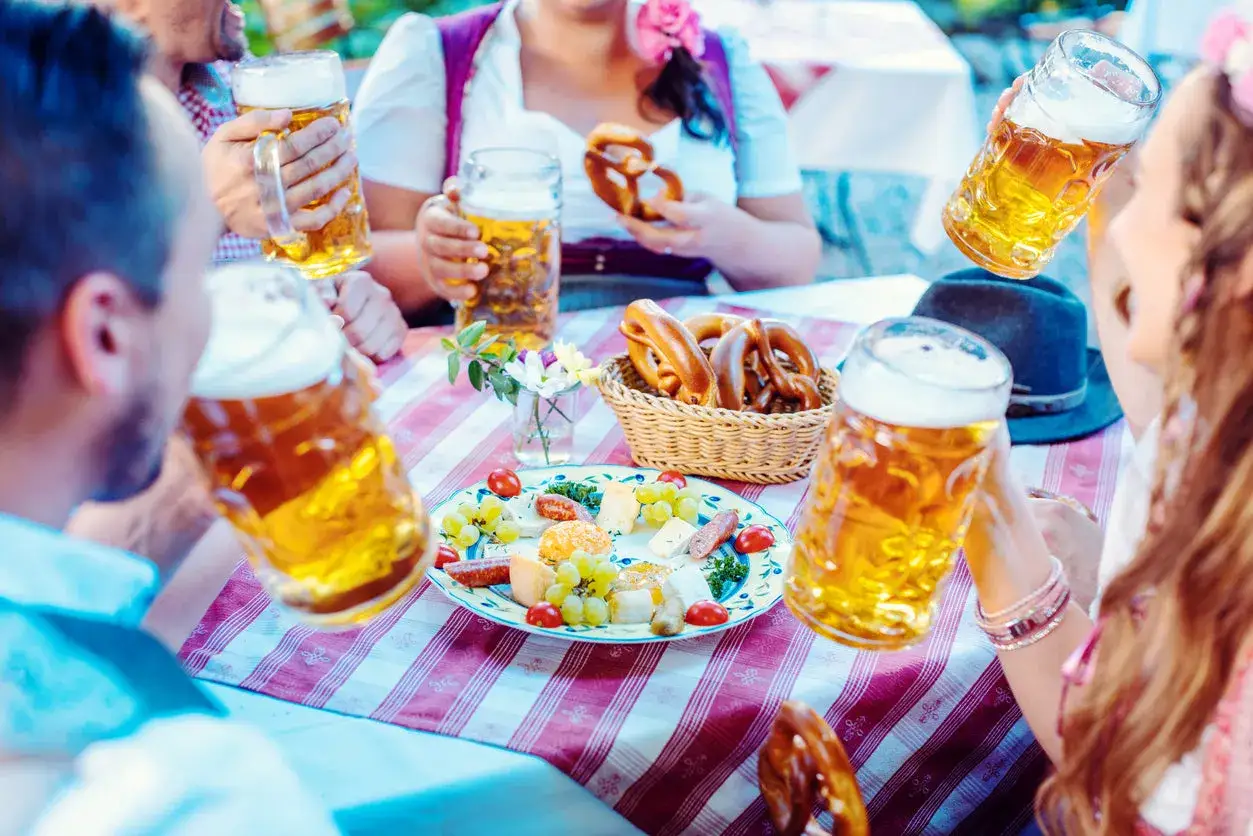 Biergarten-Stimmung mit Bierkr&uuml;gen, Brezeln im Korb und einer K&auml;seplatte.
