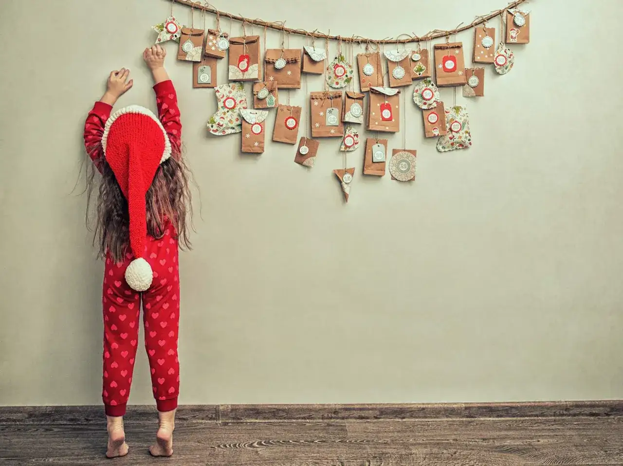Kind mit Weihnachtsmütze hängt liebevoll gestaltete Päckchen für den Adventskalender auf. Ein tolles Projekt zum Adventskalender basteln für Erwachsene!