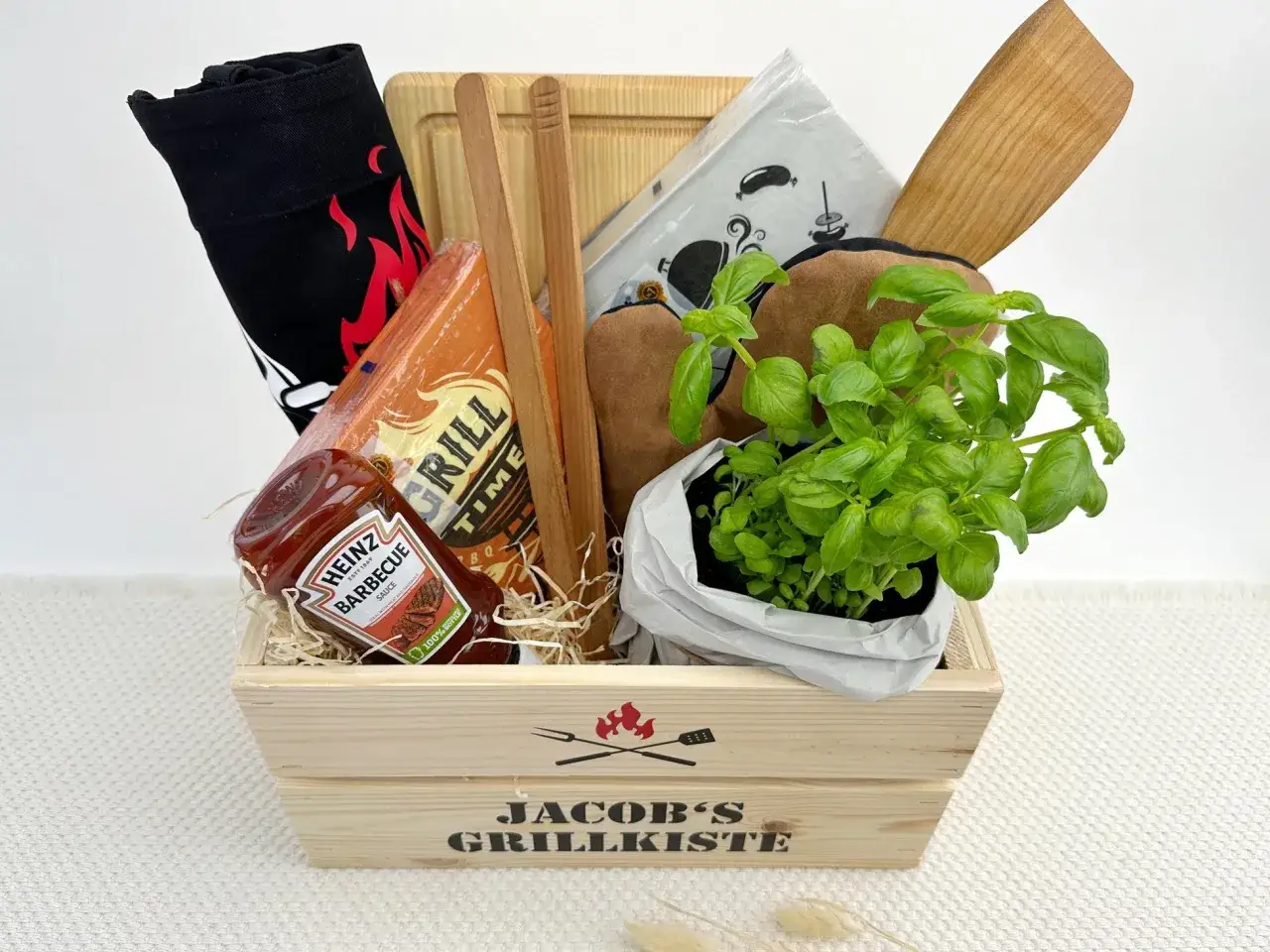 Ein toller Grill Geschenkkorb selber machen: Mit Grillzange, BBQ-Sauce, Grillhandschuhen, Brett und frischem Basilikum.