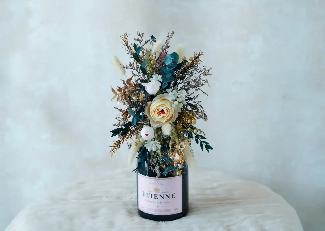 Eine Weinflasche mit Blumen verpacken: Ein Strauß aus getrockneten Blumen und Blättern schmückt eine Weinflasche mit rosa Etikett.