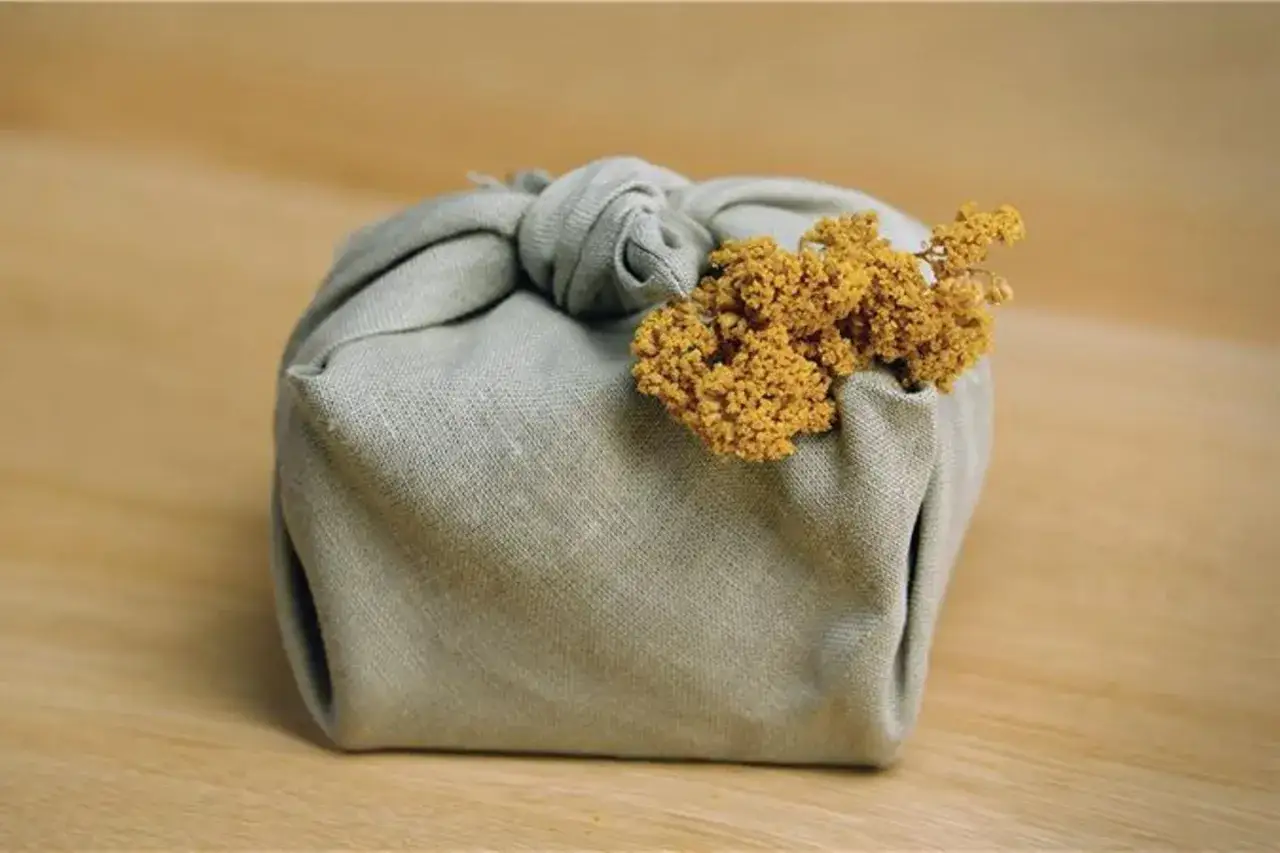 Ein Geschenk, liebevoll in Stoff gehüllt und mit getrockneten Blumen verziert. Tolle geschenke verpacken ideen für einen natürlichen Look.