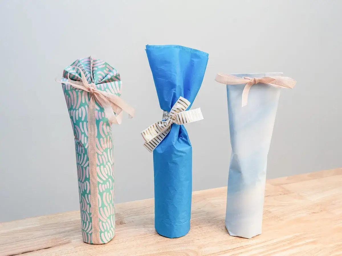 Drei schön verpackte Geschenke, die wie eine Weinflasche verpackt sind, mit Bändern verziert.