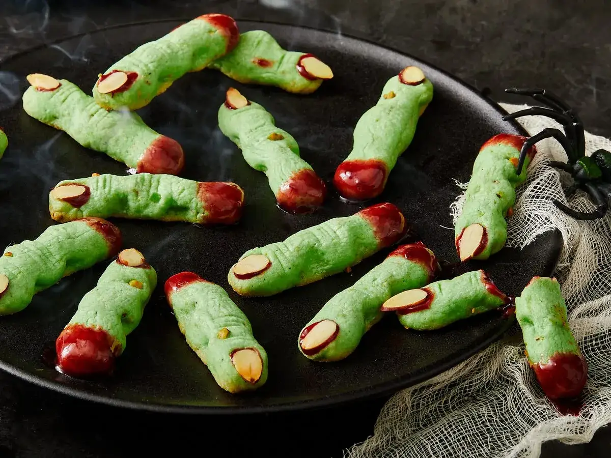 Gruselige Snacks: gr&uuml;ne Kekse in Fingerform mit Mandel-Fingern&auml;geln und rotem Zuckerguss als Blut.