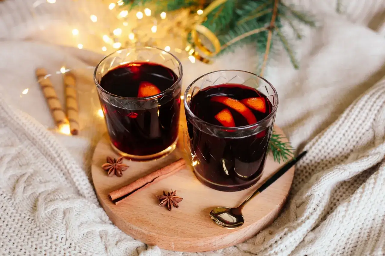Zwei Gl&auml;ser mit warmen Wintergetr&auml;nken, garniert mit Orangenscheiben, Zimt und Sternanis, umgeben von Lichterketten und einer kuscheligen Decke.