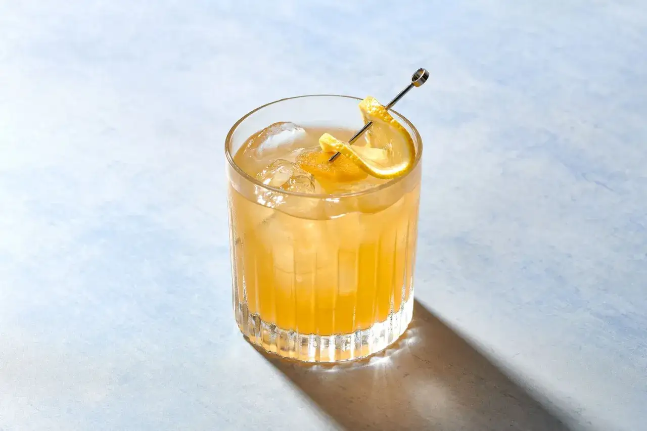 Ein goldener Penicillin Cocktail mit Eis und Zitronenspalten, garniert mit einem Spie&szlig;.