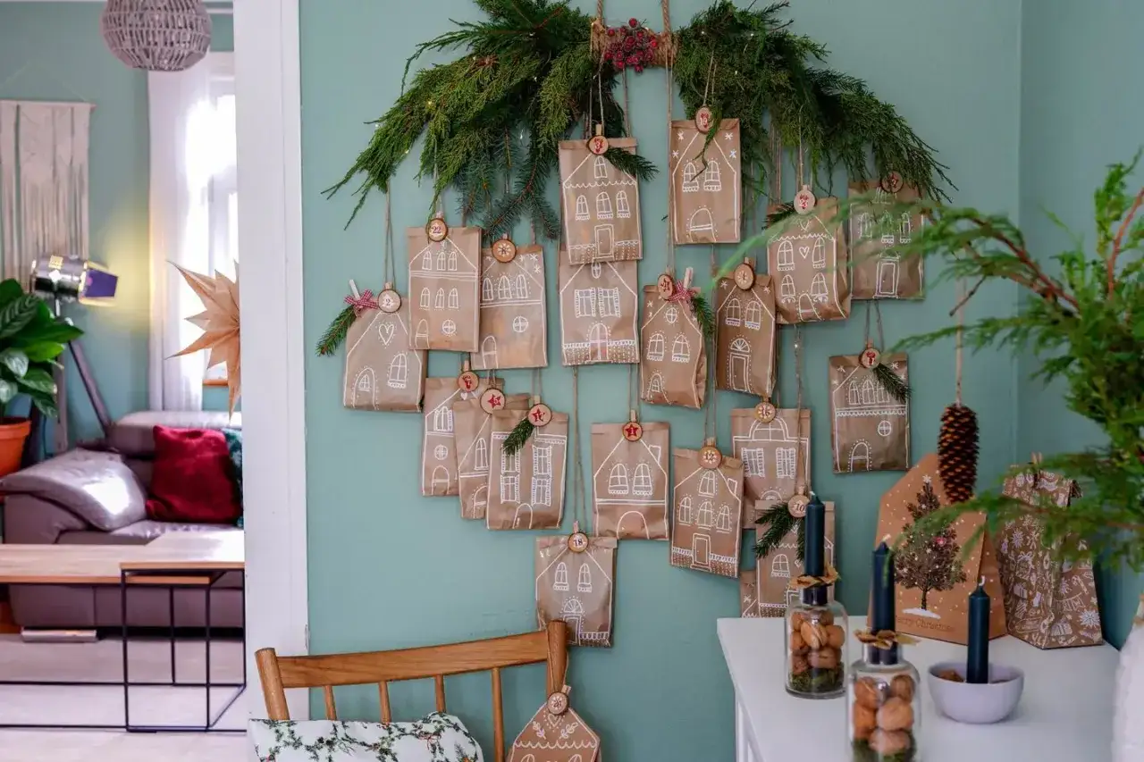 Selbstgemachte Adventskalender-Ideen f&uuml;r Frauen: Kleine Papiert&uuml;ten mit Hausmotiven, nummeriert und an Tannenzweigen h&auml;ngend, schaffen weihnachtliche Vorfreude.