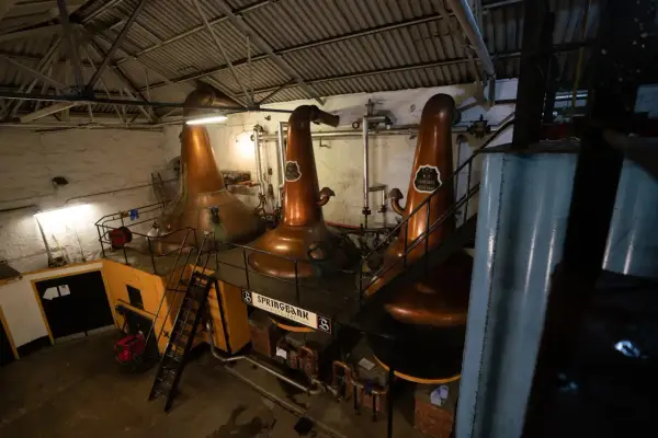 Drei große Kupfer-Brennblasen (pot still) in einer Brennerei, bereit zur Destillation.
