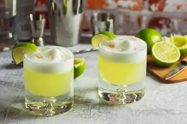 Zwei Pisco Sours mit Limettenspalten und Schaumkrone, bereit für den Genuss.